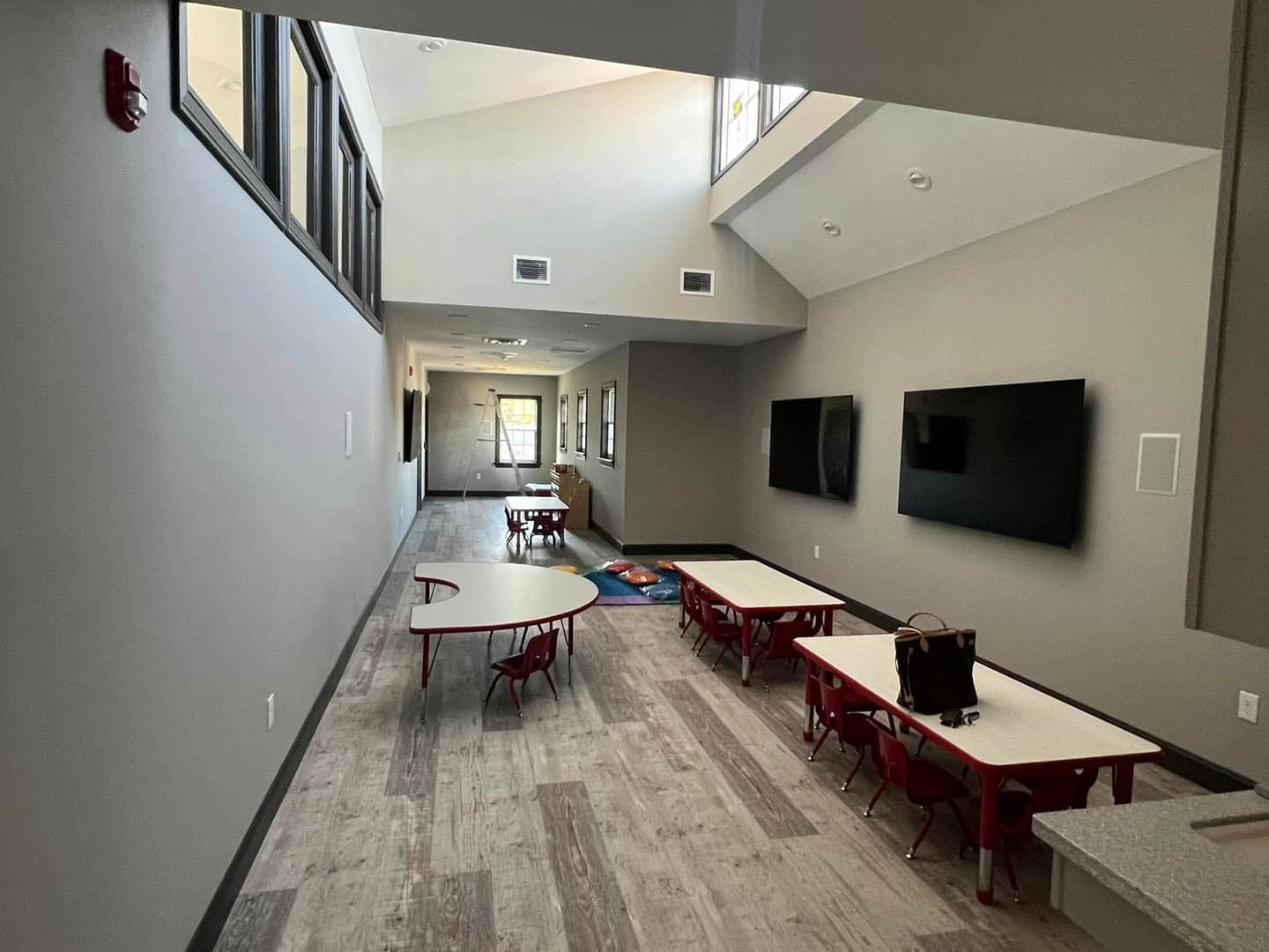 Interior of a newly completed church education wing with high clerestory windows, vaulted ceiling, light wood-look flooring, and red children's chairs with curved tables
