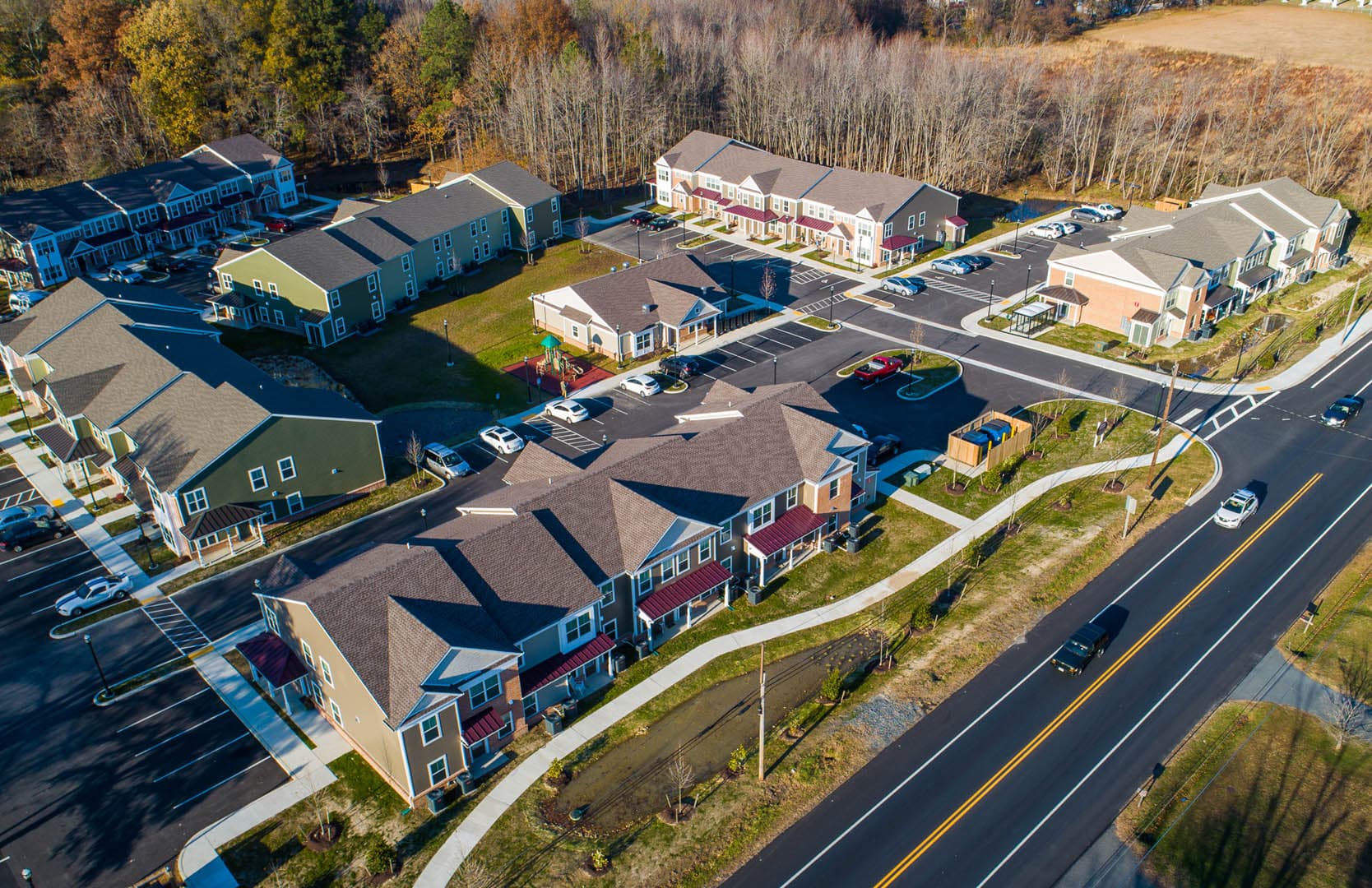 Aerial view of a mixed-use residential development featuring townhomes, apartment buildings, and a commercial pad site along a main road