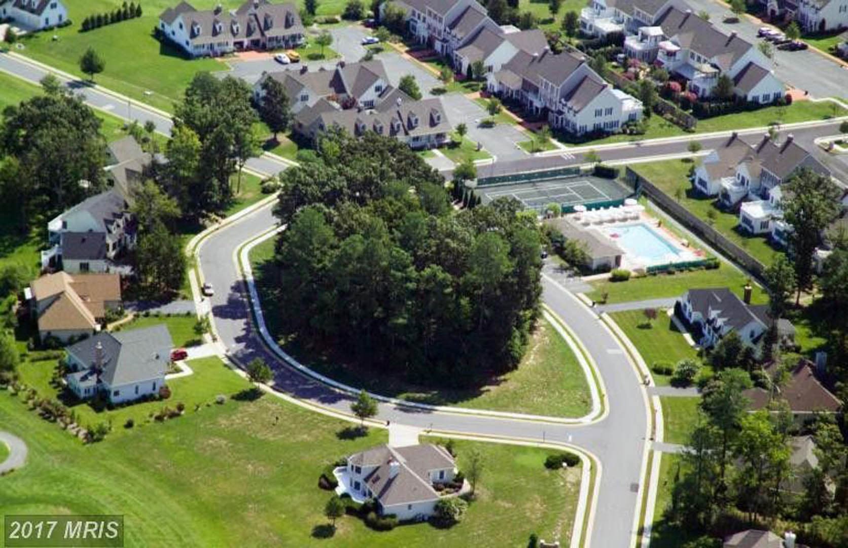Aerial photograph of an established residential subdivision with curving streets, a community pool, tennis courts, and mature tree canopy