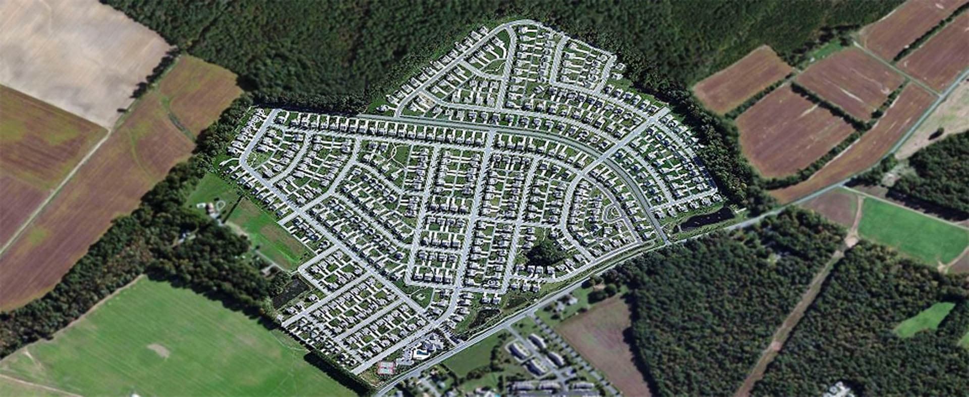 Oblique aerial view of a large residential subdivision with a dense grid of streets and homes surrounded by agricultural fields and woodlands