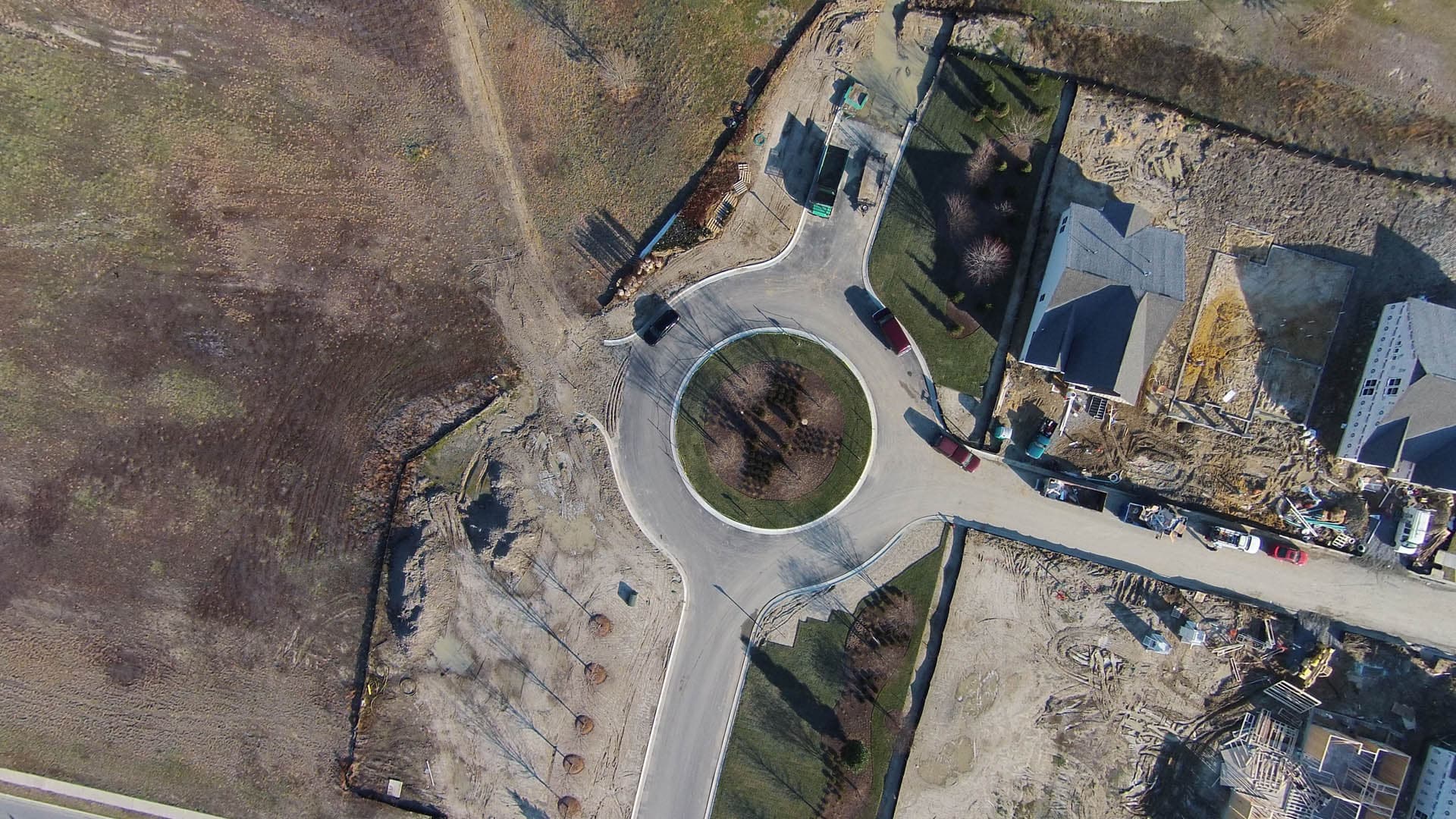 Aerial view of a newly constructed residential street roundabout with a circular landscaped center island, surrounded by active home construction