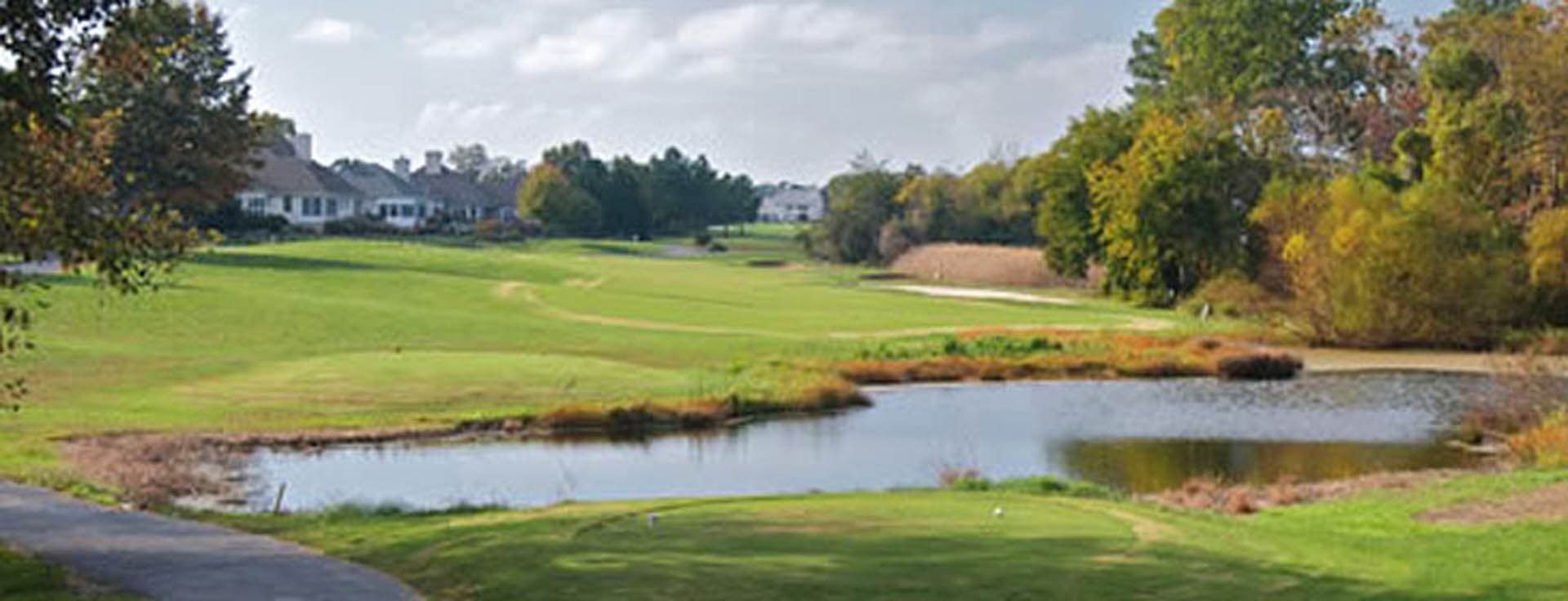 Golf course fairway with a water hazard pond and natural marshy vegetation in autumn colors, with residential homes in the background