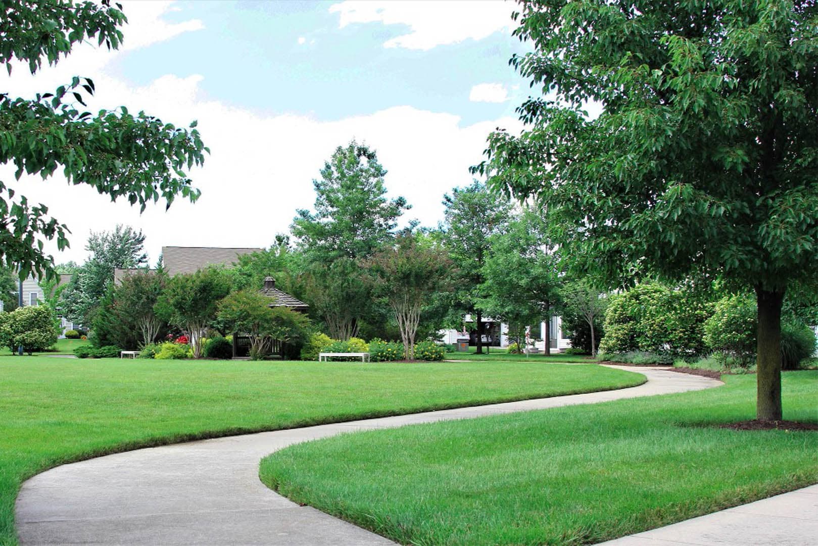 Winding concrete sidewalk curving through a well-landscaped residential common area with mature crape myrtles, shrubs, and open lawn