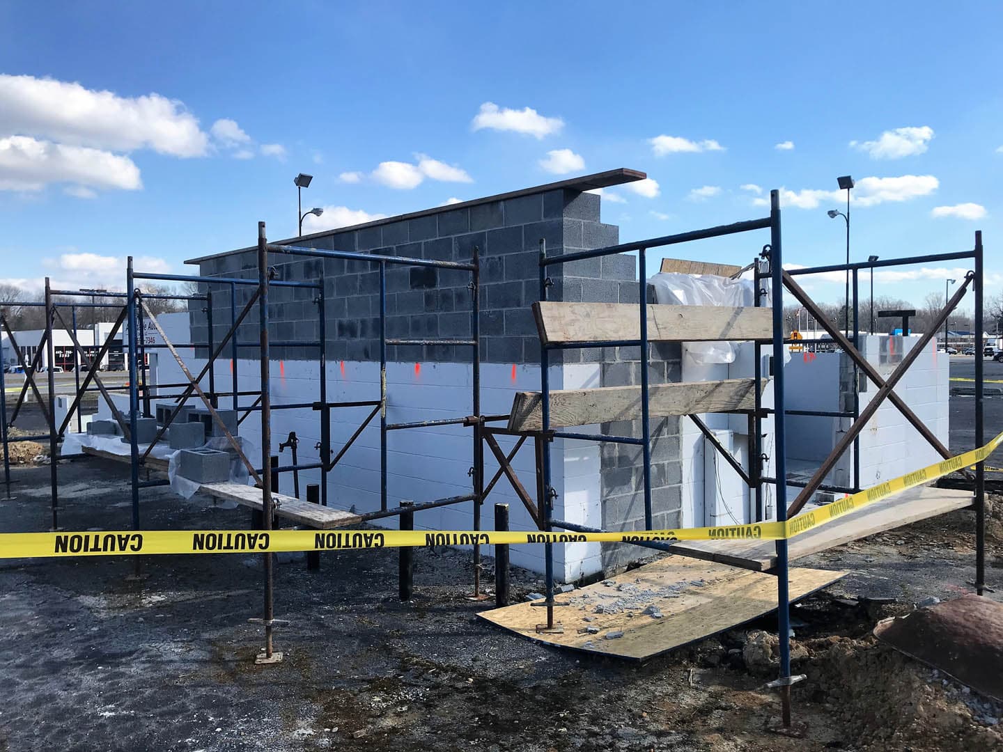 Concrete masonry unit block walls under construction surrounded by steel scaffolding and yellow caution tape at a commercial building site