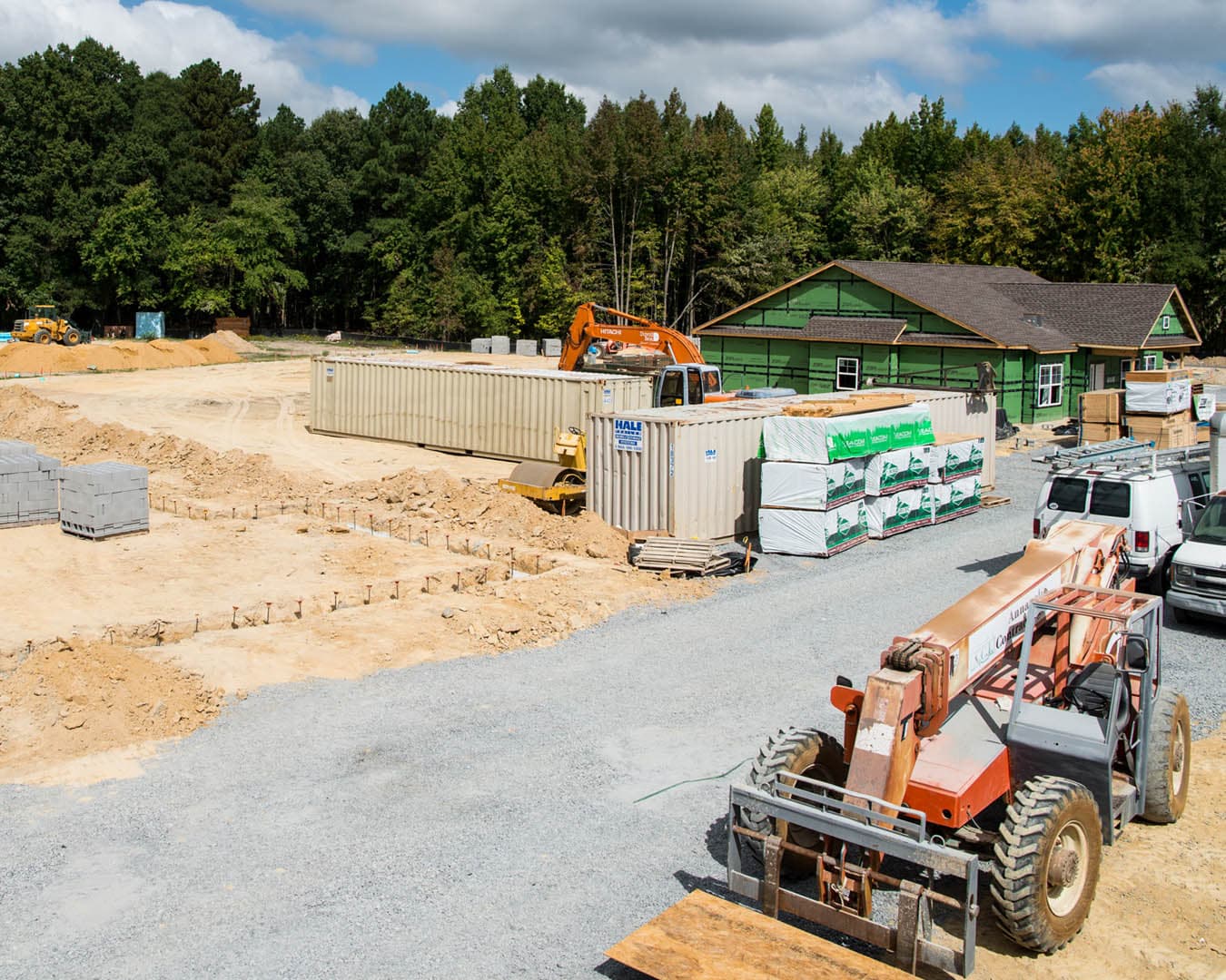 Active commercial construction site with concrete masonry block foundation footings, a shipping container, and a partially framed building in the background