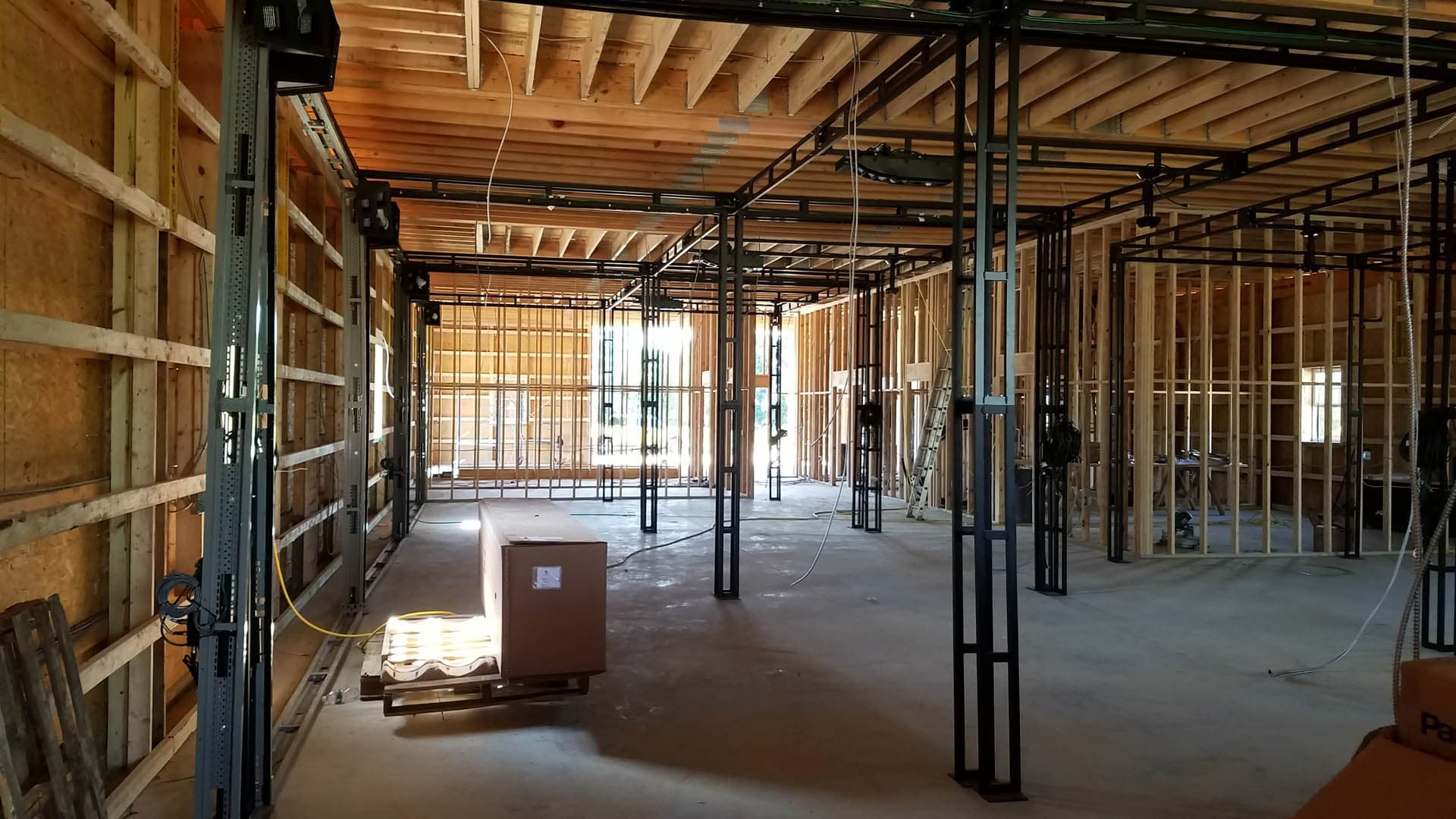 Interior of a commercial building under construction showing exposed wood roof trusses, steel column framing, metal stud walls, and electrical conduit rough-in