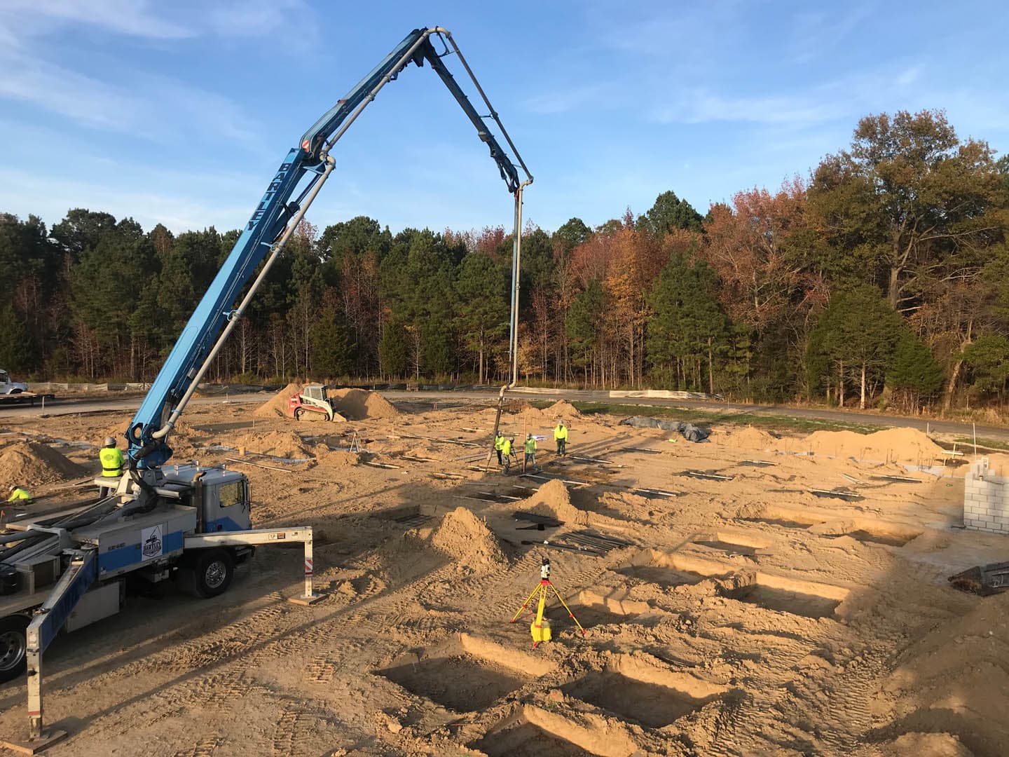 Large blue concrete pump boom truck extending over a building site as workers guide the pour during foundation slab construction