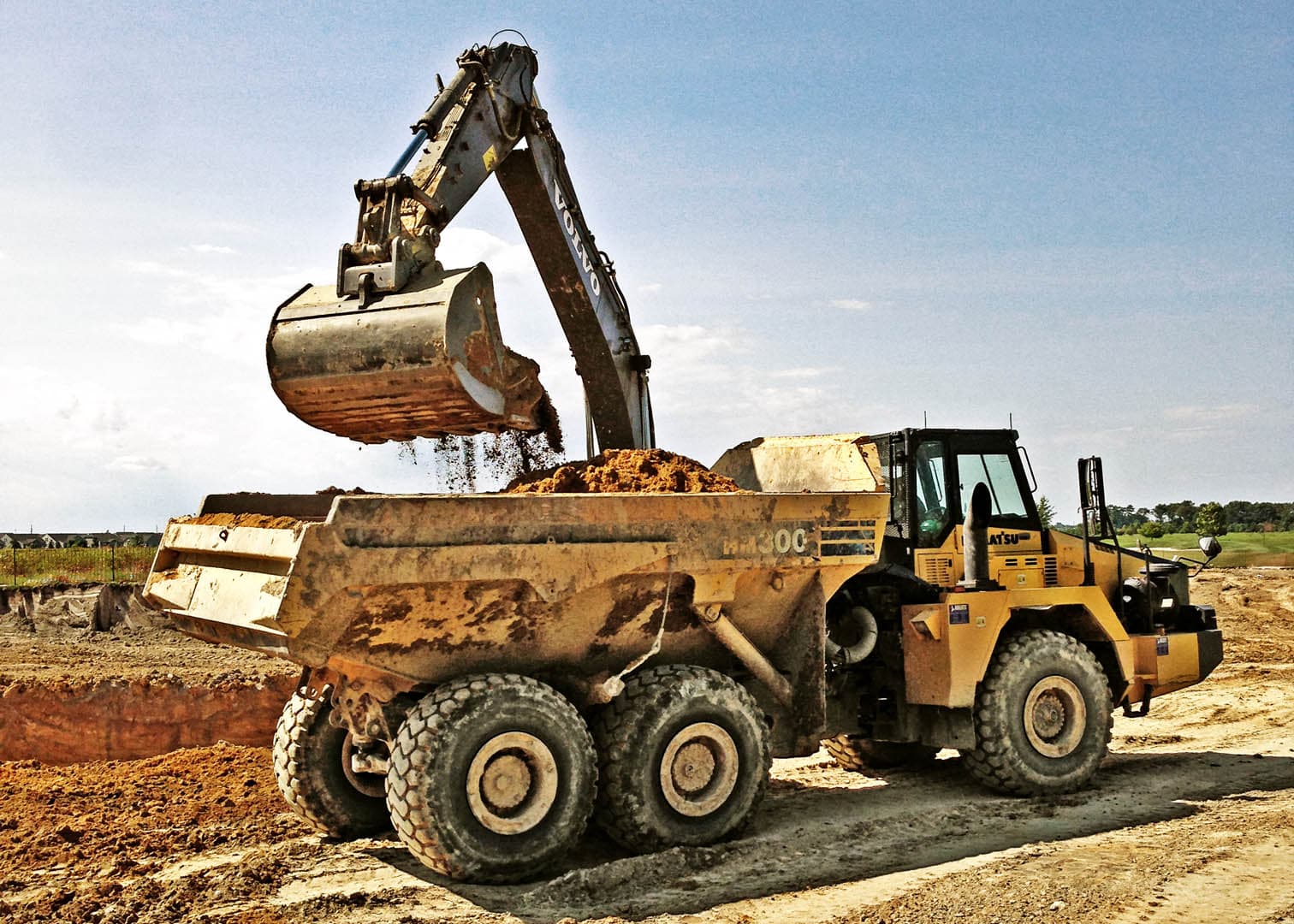 Excavator loading sandy soil into a Komatsu articulated dump truck during mass grading operations at a commercial construction site