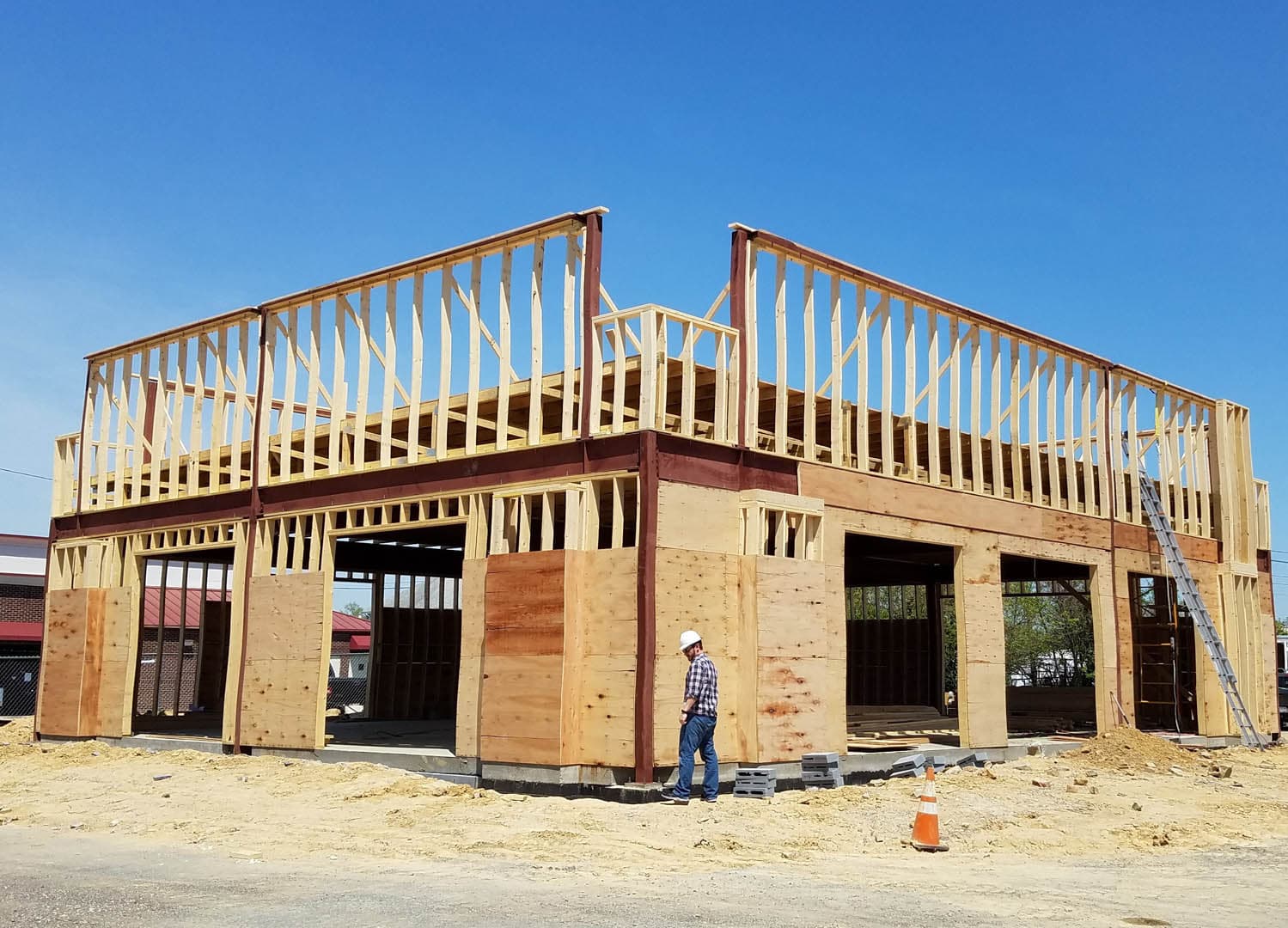Construction manager in a hard hat inspecting a two-story wood-framed commercial building with open stud walls and second-floor deck framing