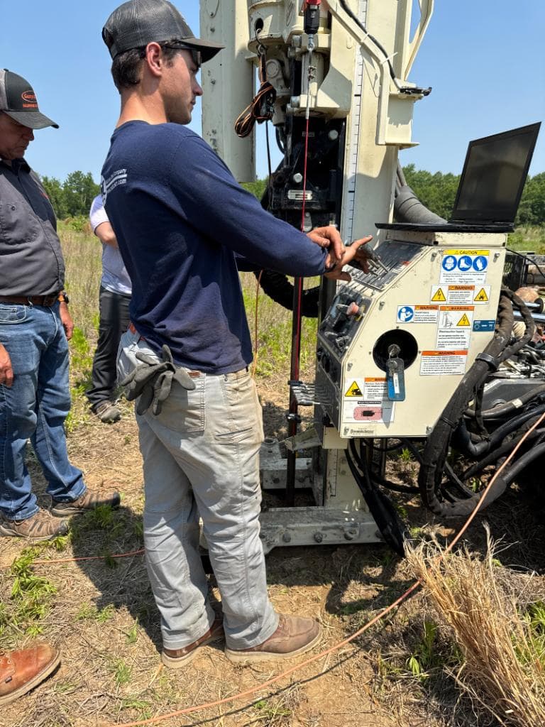 RAUCH environmental technician operating Geoprobe direct-push drilling rig controls at an outdoor field investigation site