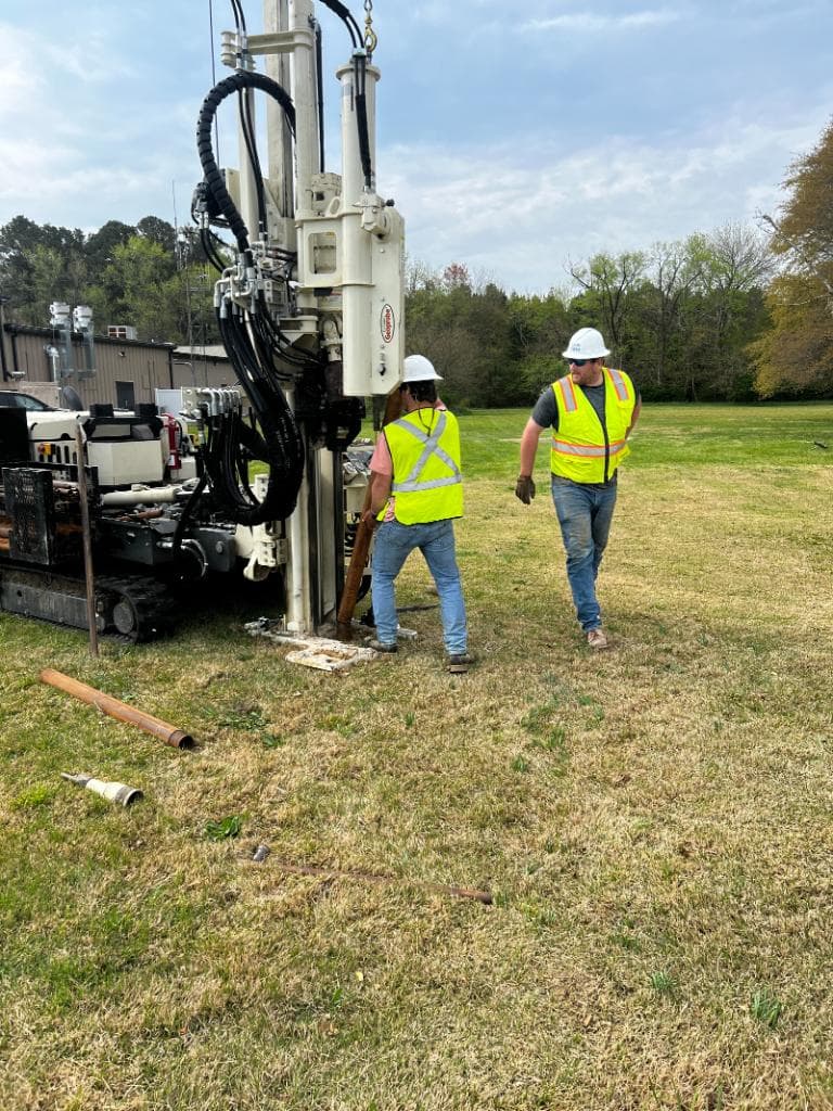 Two technicians operating a drill rig for well installation in an open field