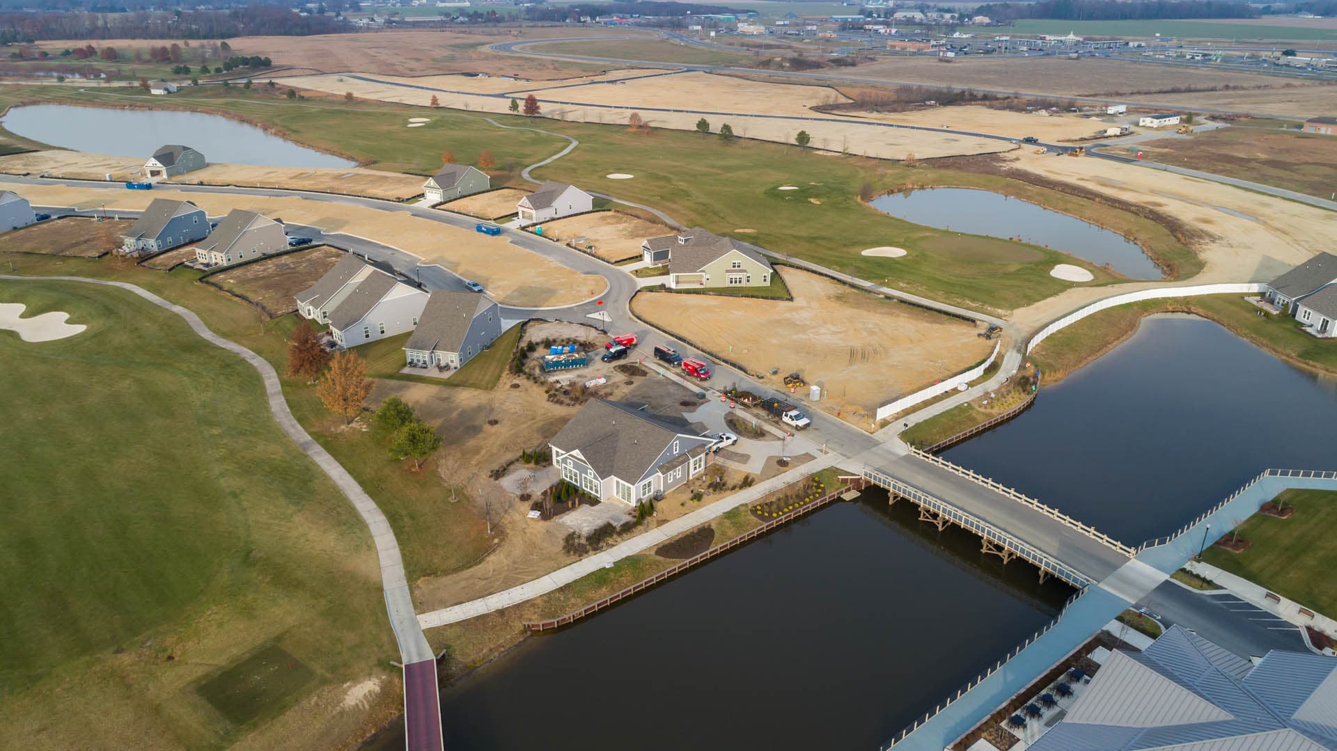 Wide aerial drone photograph of a large mixed-use golf course community showing a canal with a vehicle bridge, clustered residential homes, and retention ponds