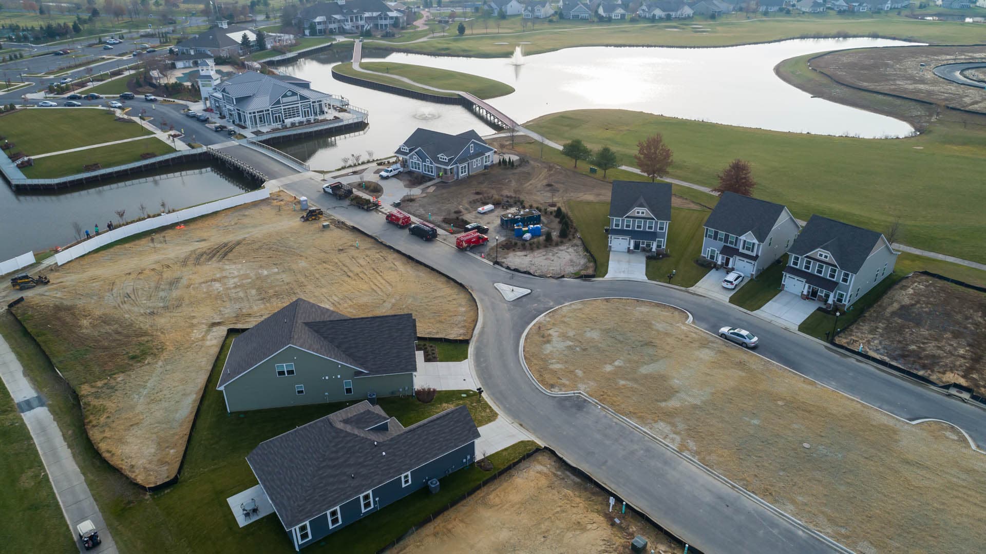 Aerial drone photograph of a mixed residential and golf course community under construction, featuring a stormwater pond with fountain and a cul-de-sac