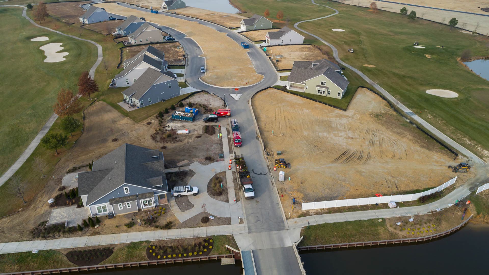 Aerial drone photograph of an active residential construction site adjacent to a golf course, showing graded lots, construction equipment, and a waterway