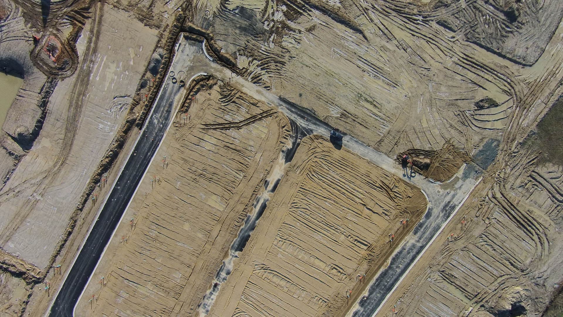 Straight-down aerial drone photograph of graded earthwork lots at an active construction site, showing tiered cut-and-fill slopes and heavy equipment tracks
