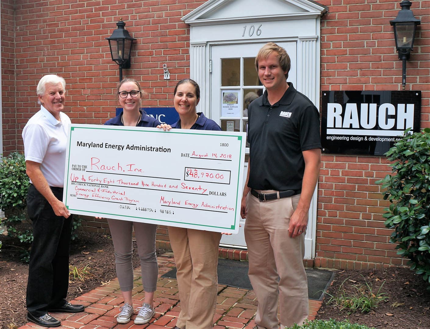 Four people standing outside the RAUCH Inc. office holding a ceremonial check from the Maryland Energy Administration for $48,930