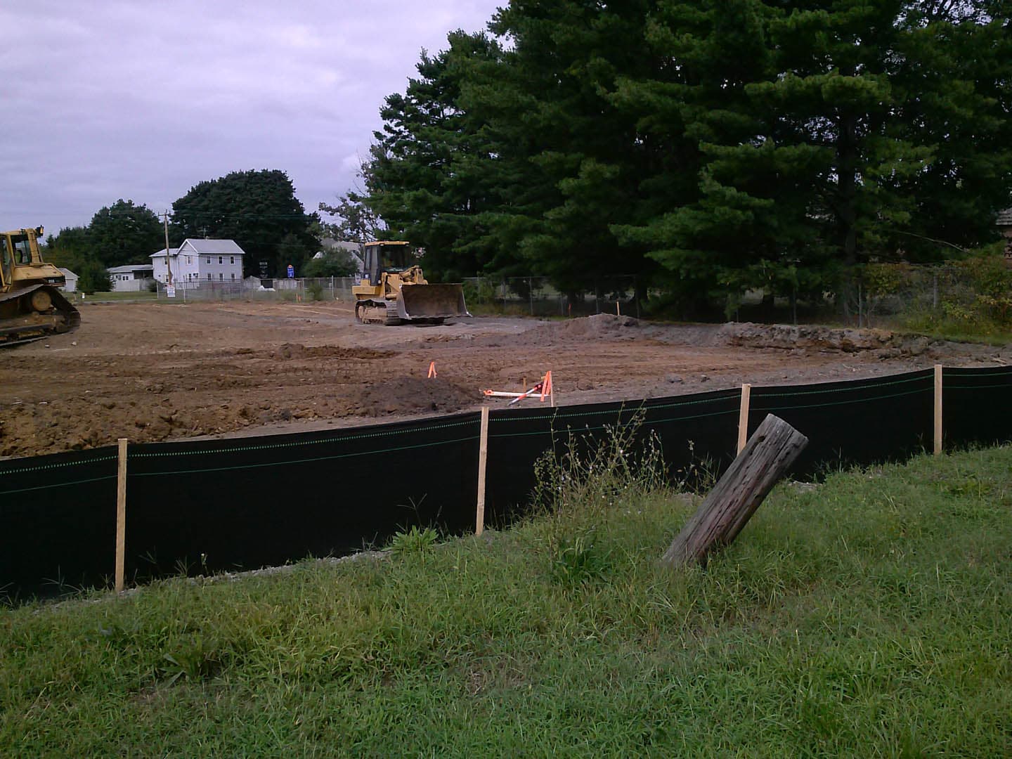 Graded and cleared construction site with a silt fence installed along the perimeter and a bulldozer actively pushing soil in the background