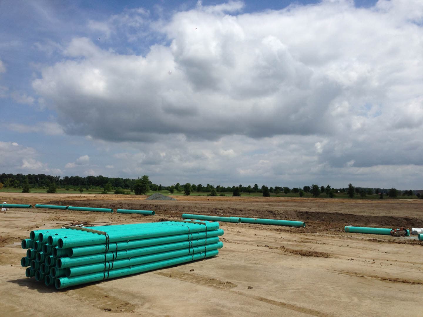 Bundles of green PVC water main pipes staged on a large graded earthen site ready for installation