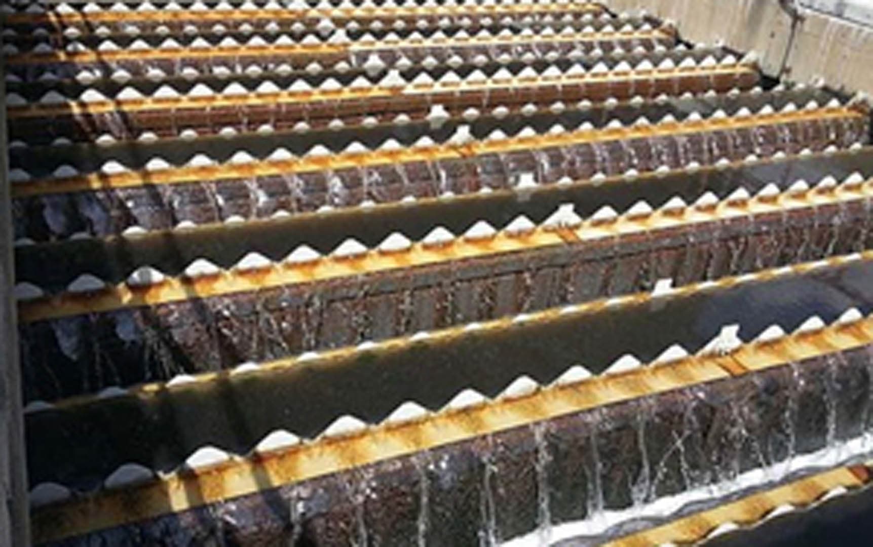 Close-up view of a trickling filter clarifier showing rows of serrated metal baffles with wastewater flowing and biological growth