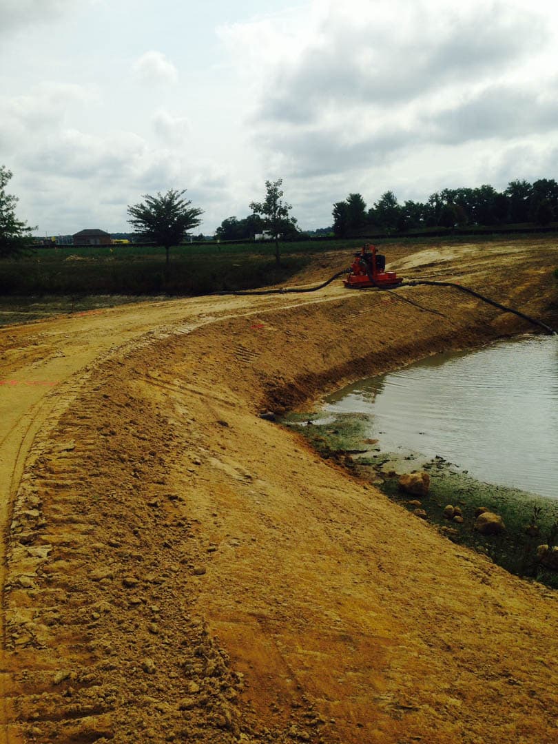 Heavy equipment pumping water from a partially filled wastewater lagoon along a freshly graded earthen berm during construction