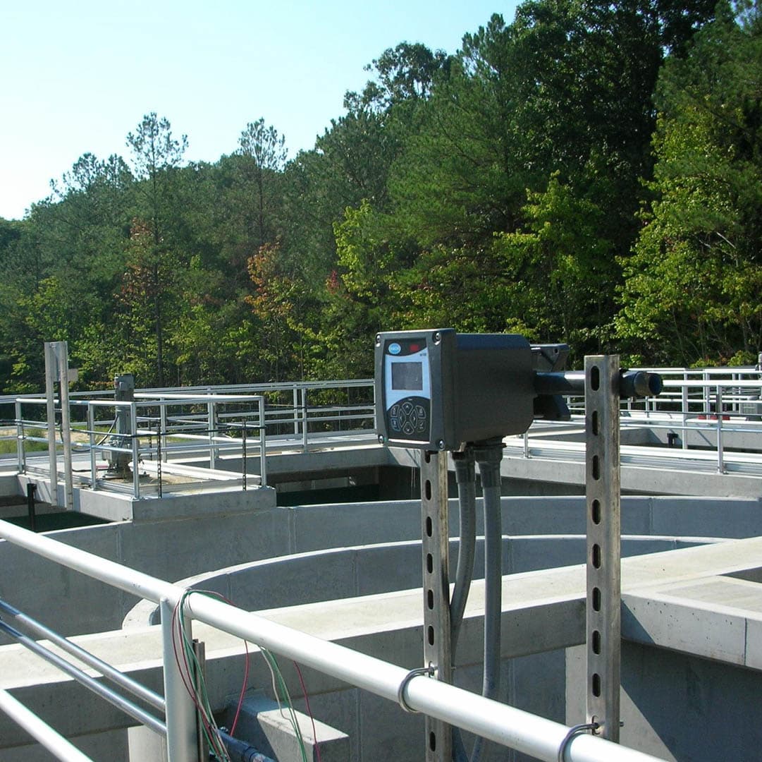 Outdoor wastewater treatment clarifier tanks with stainless steel walkway railings and an electronic water quality monitoring instrument