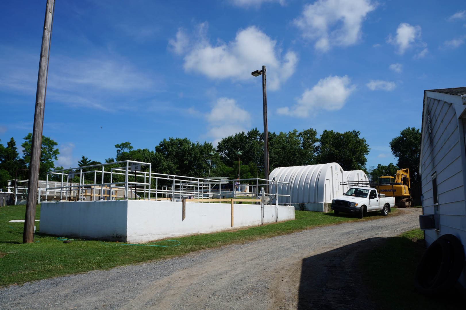 Wastewater treatment plant undergoing upgrades with open concrete aeration basin framing and a Komatsu excavator on site